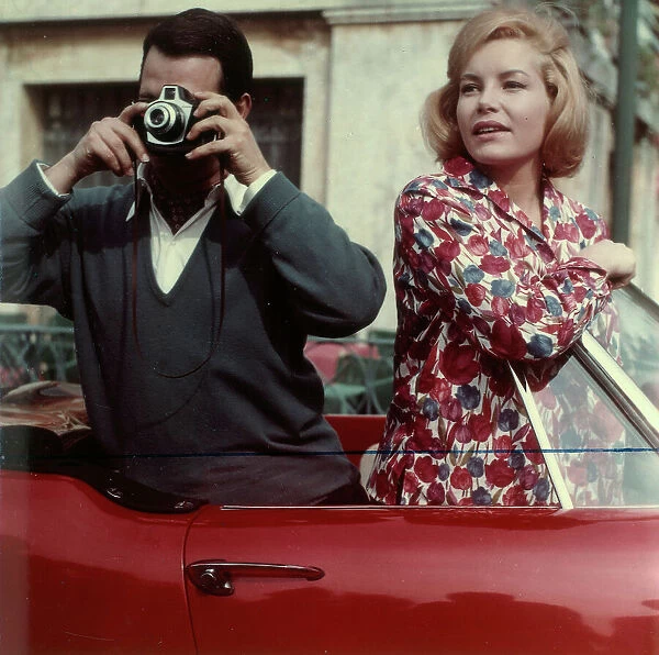 Man taking pictures from a car accompanied by a woman