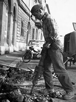 Images Dated 24th March 2011: A construction worker with a jack hammer as digs a trench in the road