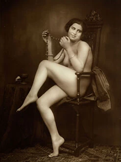 Images Dated 29th October 2010: Female nude: young lady, sitting on a chair, shows a necklace which she keeps on her hands