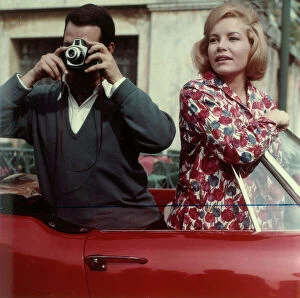 : Man taking pictures from a car accompanied by a woman