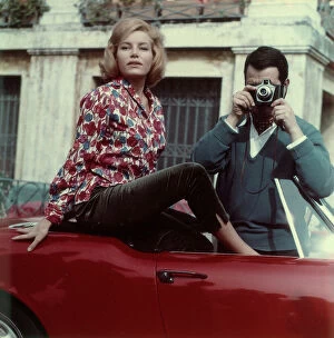 : Man taking pictures from a car accompanied by a woman